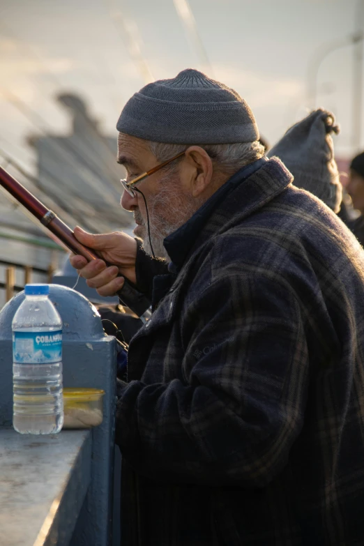 an old man holding a fishing rod looking at a water bottle