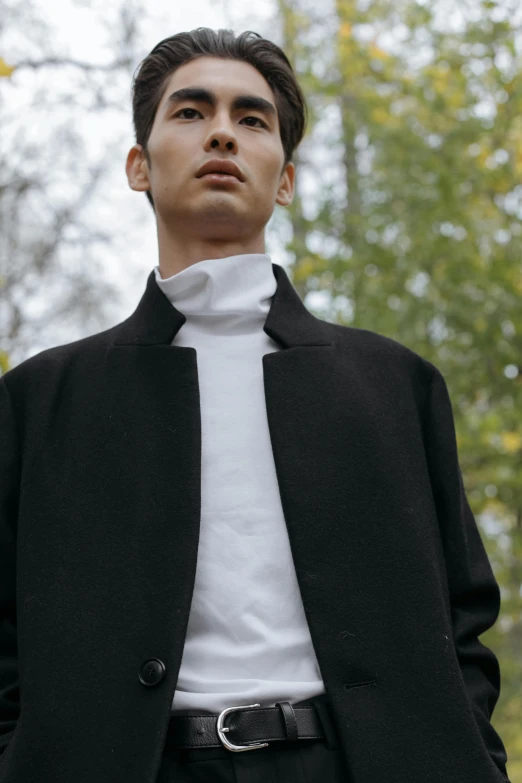 a young man poses with his suit jacket over and a white turtleneck sweater underneath