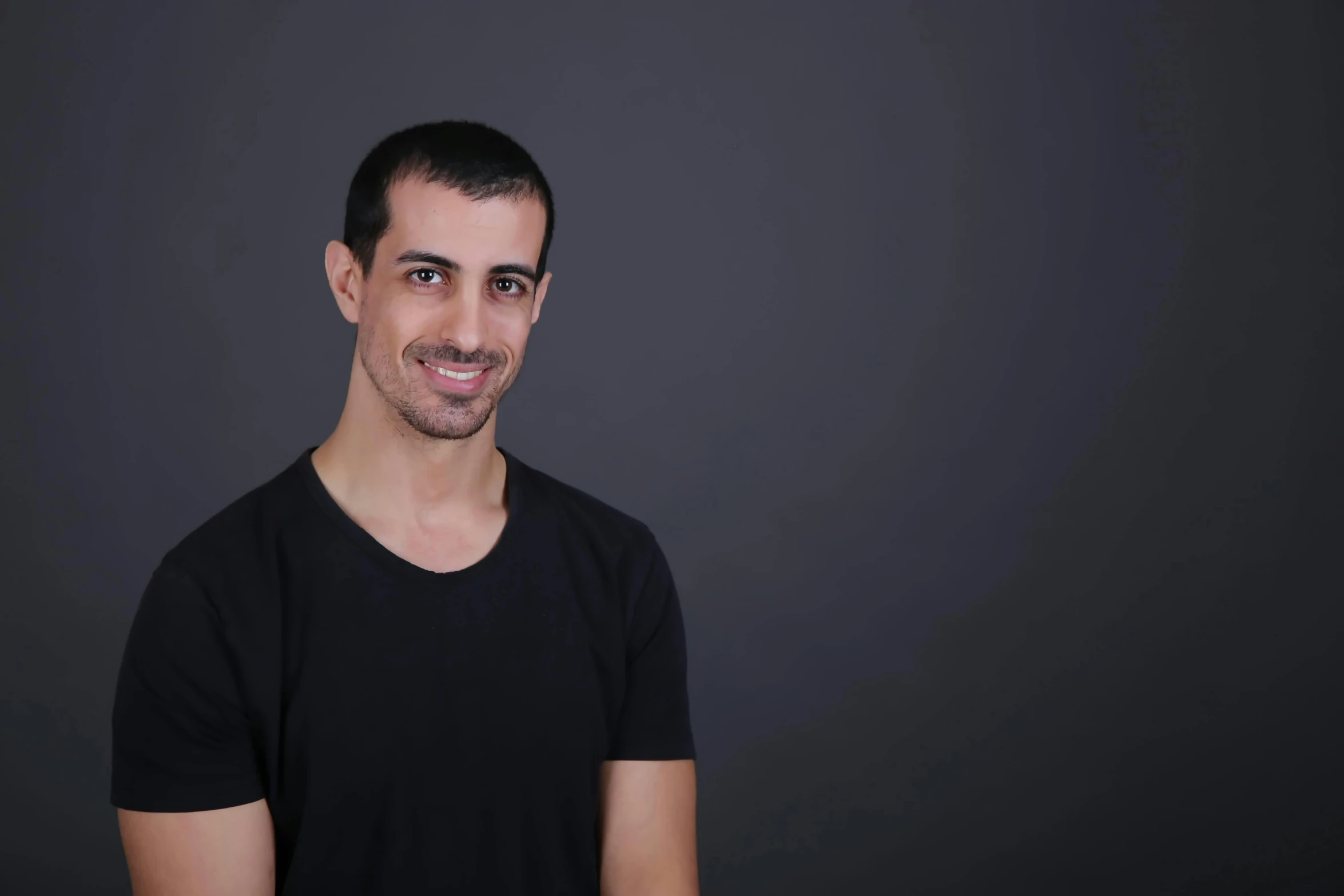 a man smiling with a black shirt and black wall