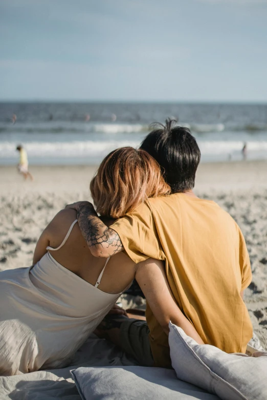 two people are sitting on a blanket together at the beach