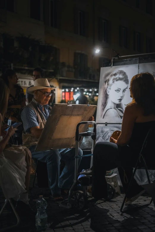 several people sit outside as a man works on a picture