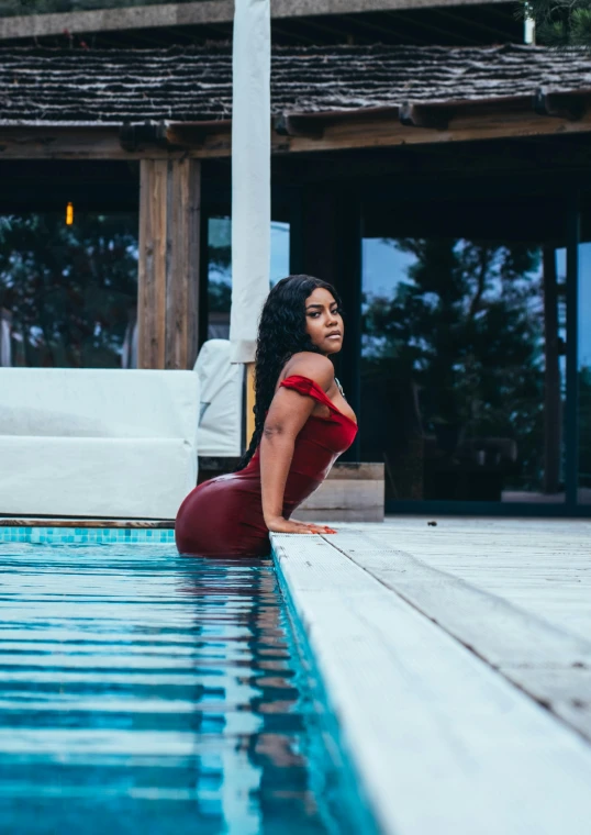 a woman in a red dress is sitting on a ledge by the water