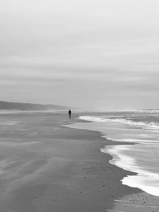 a lone man walking on an empty beach near the ocean