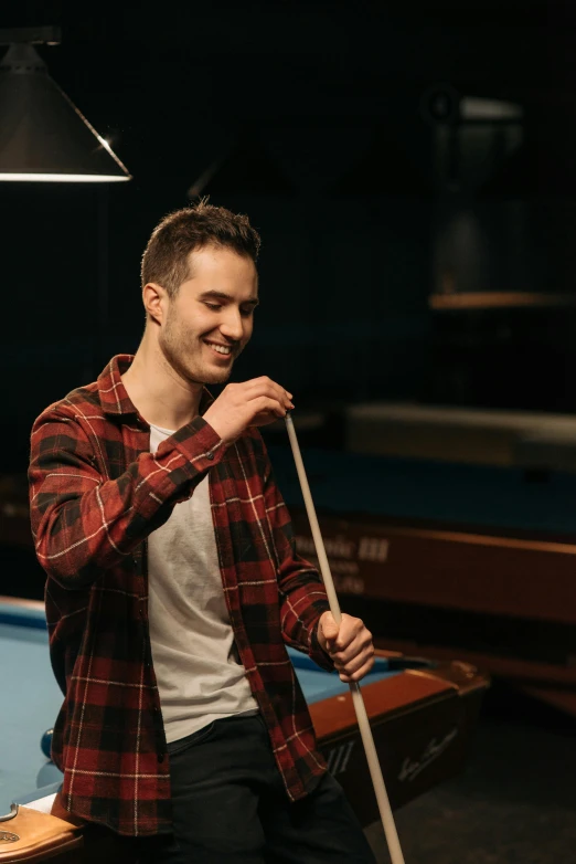 a smiling man leans up against a pool table