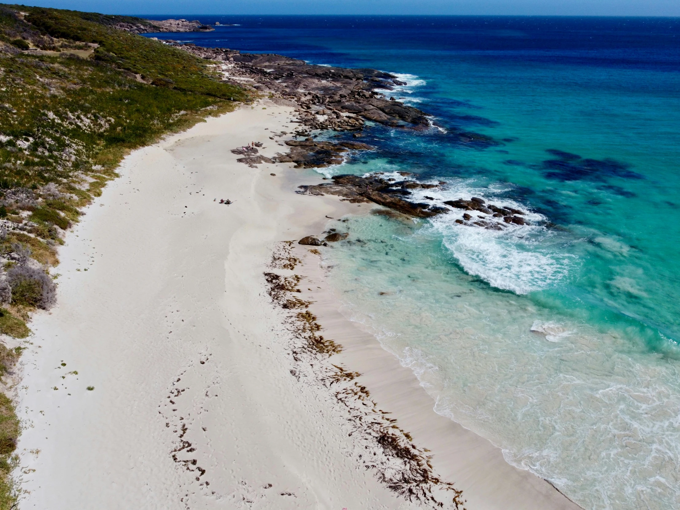 an aerial view of a beach with sand, bushes and blue water