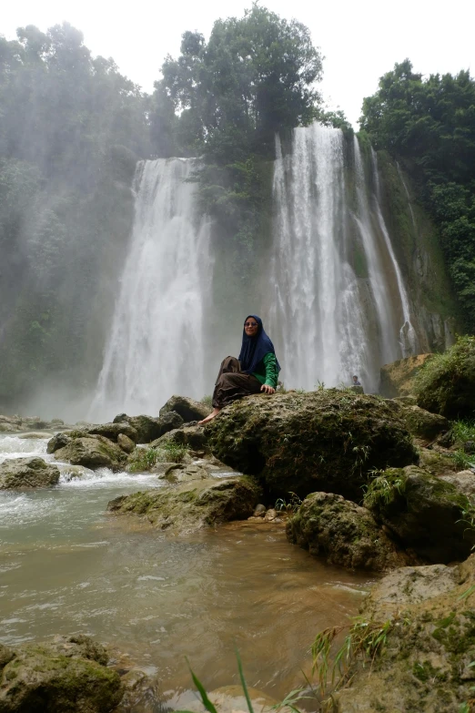 the person is posing in front of a very tall waterfall