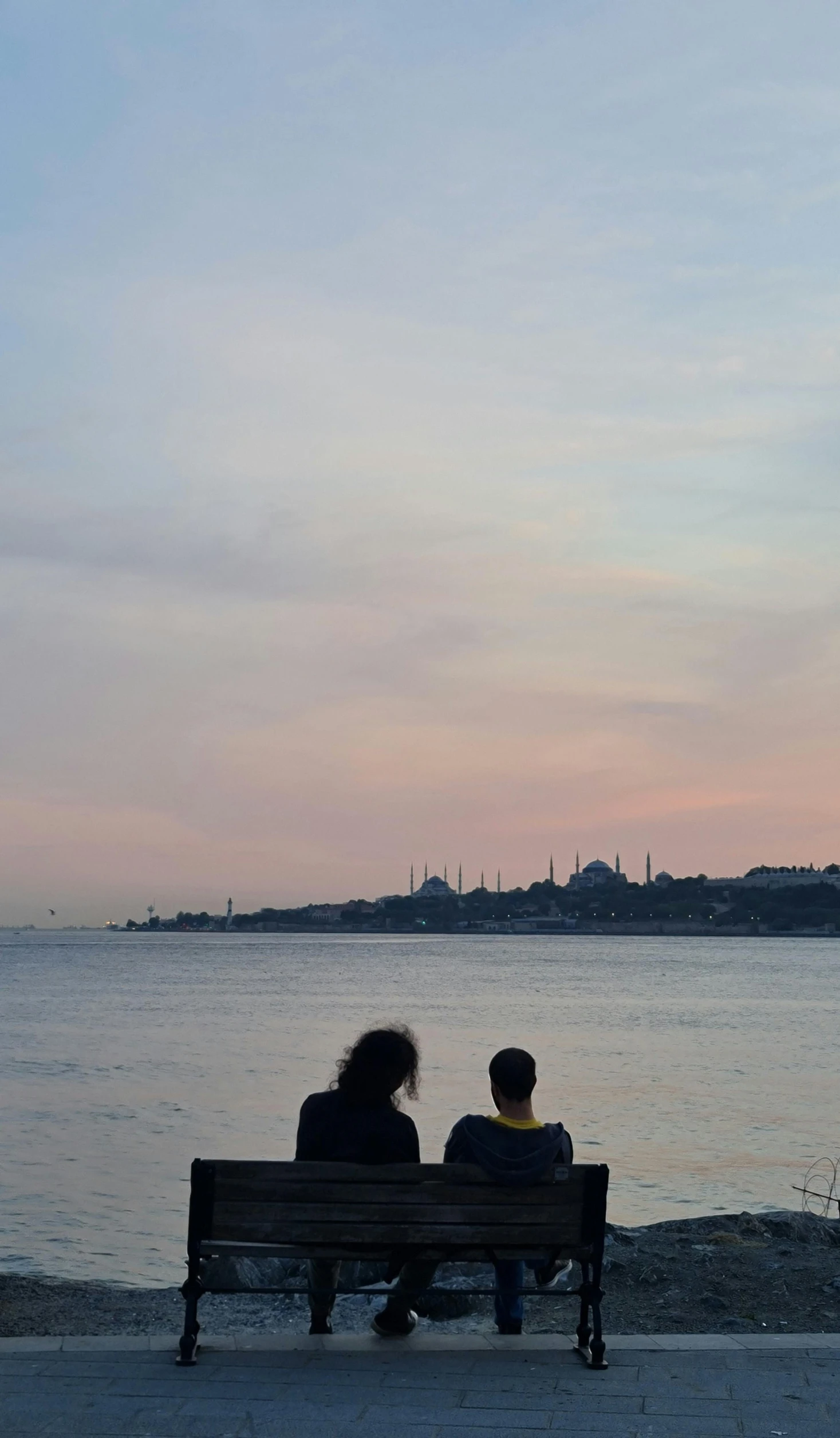 two people sitting on a bench next to a large body of water