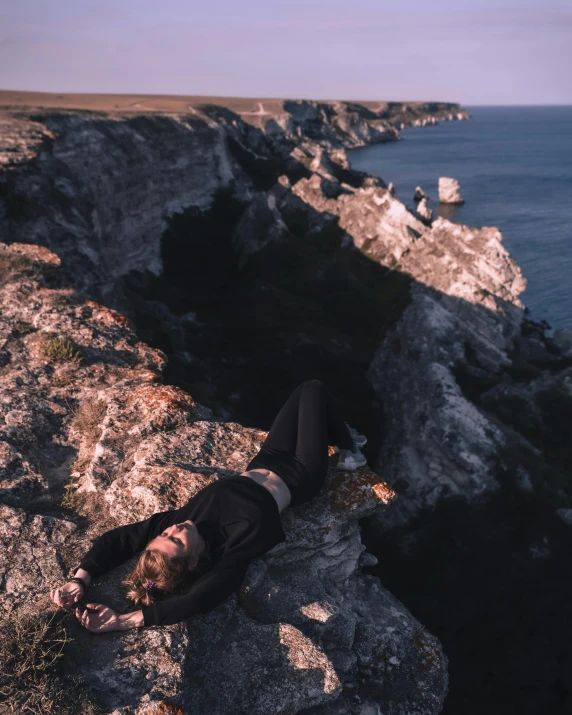 a person laying on top of a large rock next to the ocean