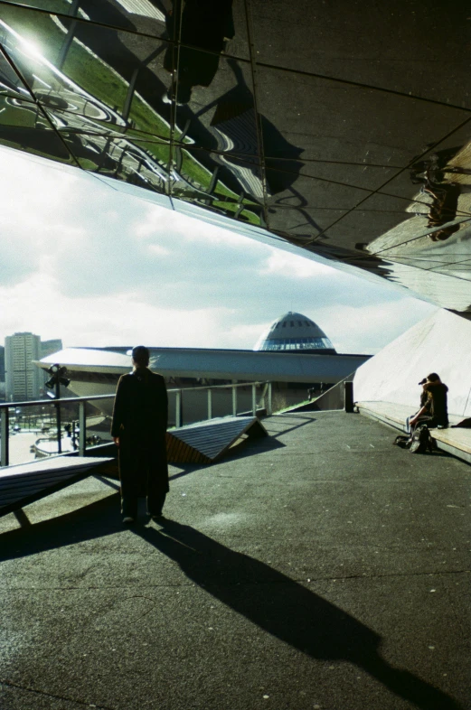 man standing in front of large reflective mirror while people sit outside