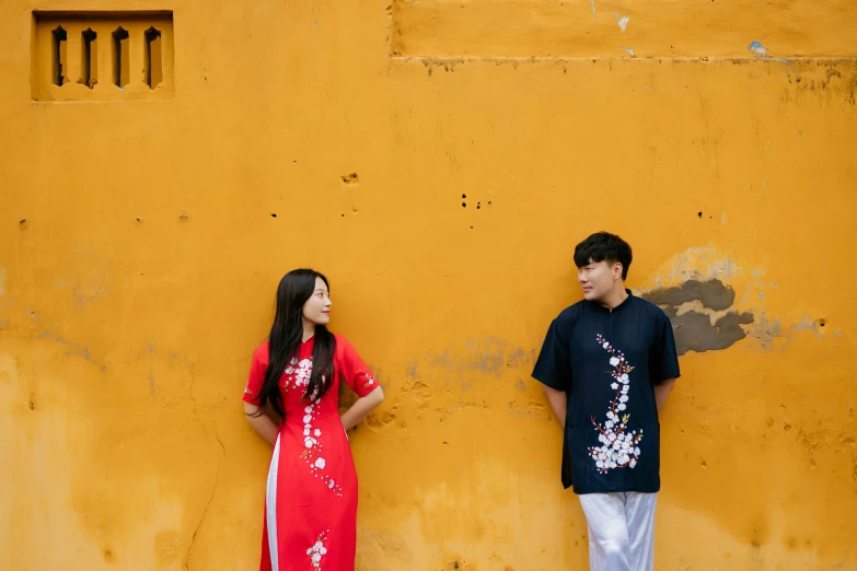 two people standing against a yellow wall with flowers on them