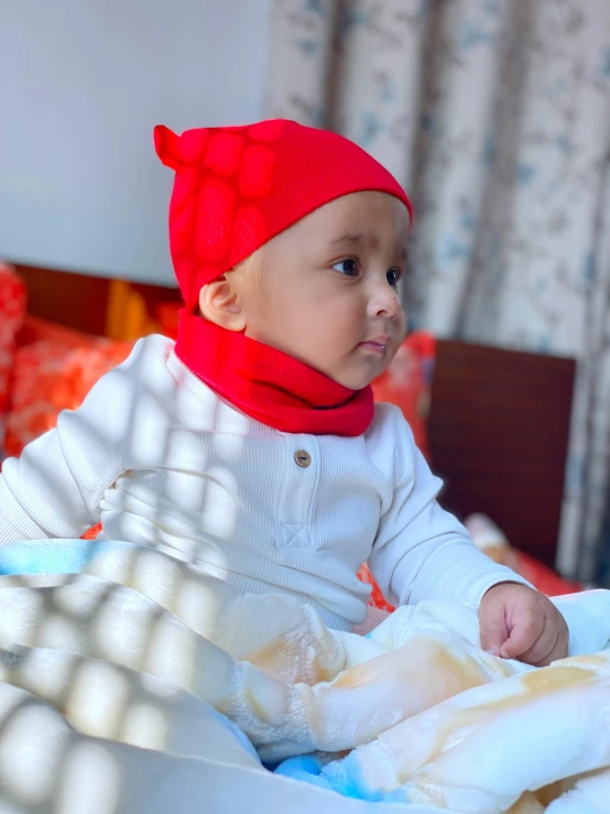 a little baby in a red hat on top of a bed