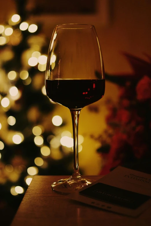 a wine glass sitting on a table with a lit christmas tree in the background