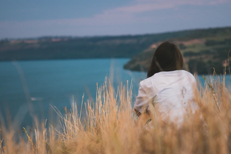 the woman sits near a lake looking off into the distance