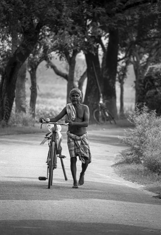 an old man walks with his bicycle down the road