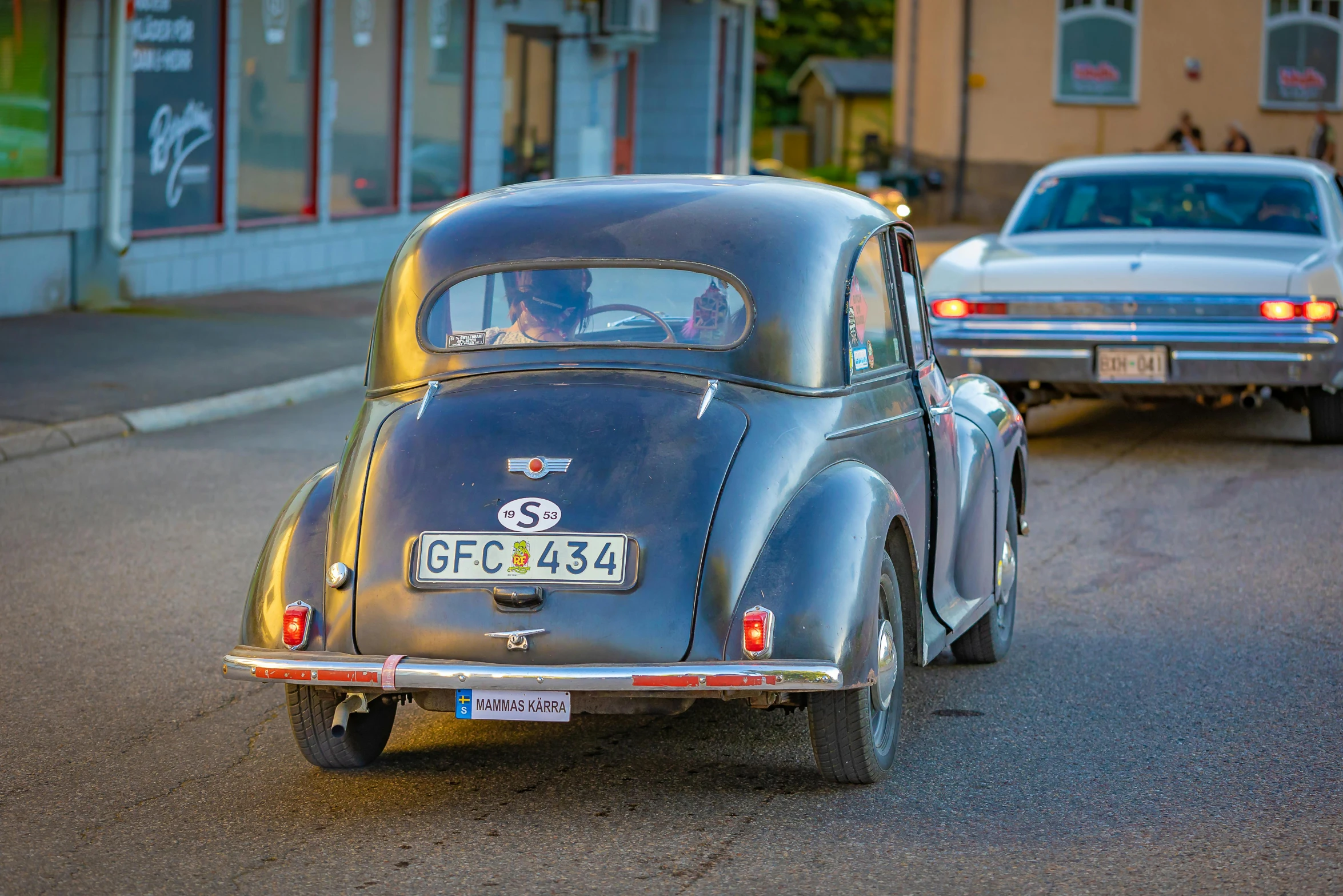 a classic car driving down the road behind another one