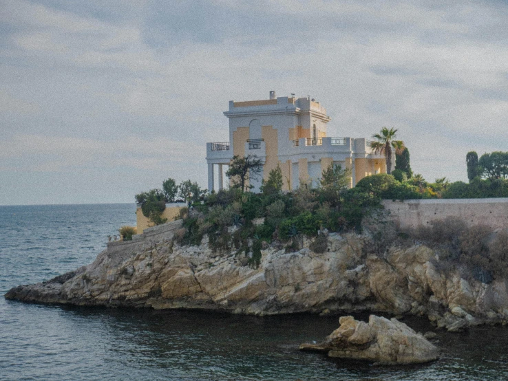 a white house with a balcony sits on the shore of the ocean
