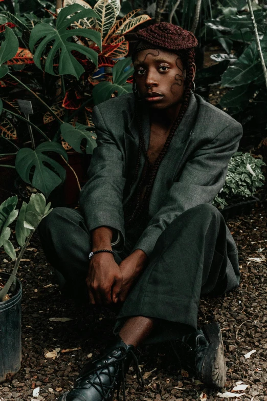 the man is wearing a brown hat and sits in front of plants