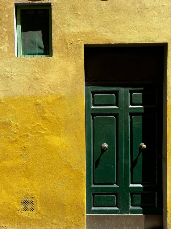 the outside of a yellow building with a green door and two windows