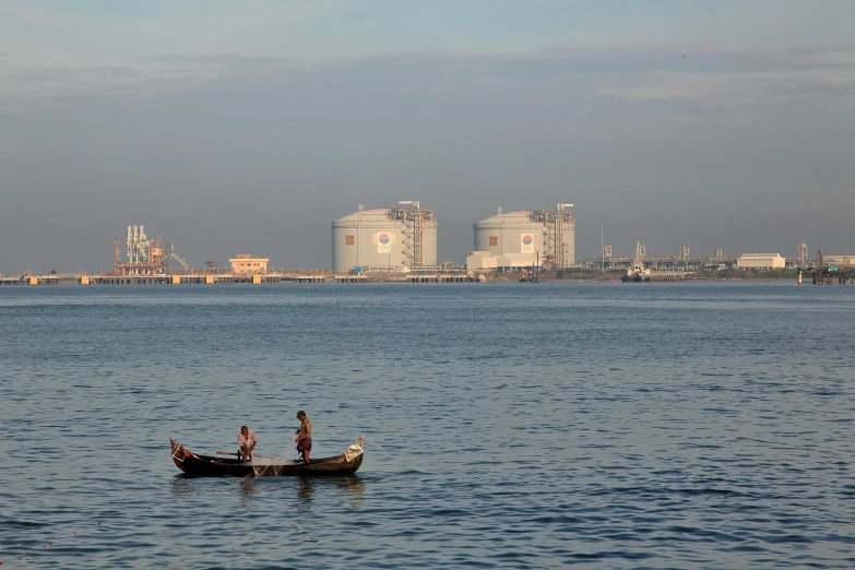 two men in a boat and oil refinerys in the distance