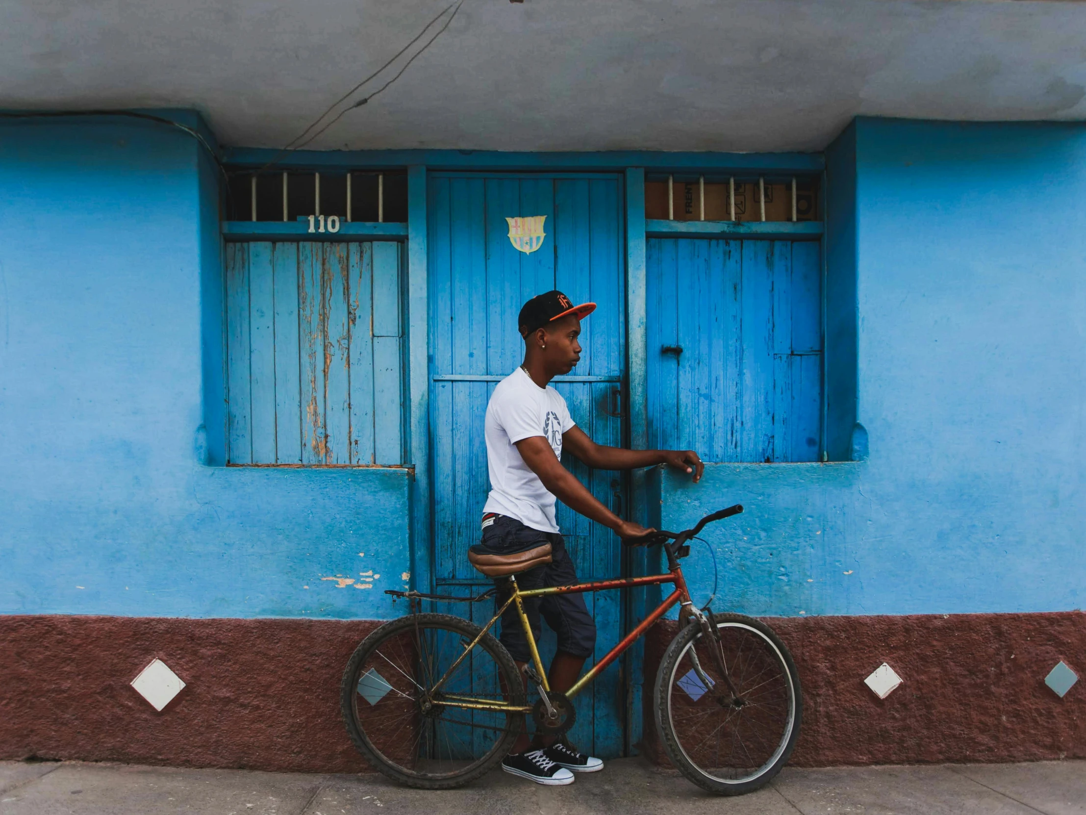 man standing in front of blue painted building with bike leaning on the door