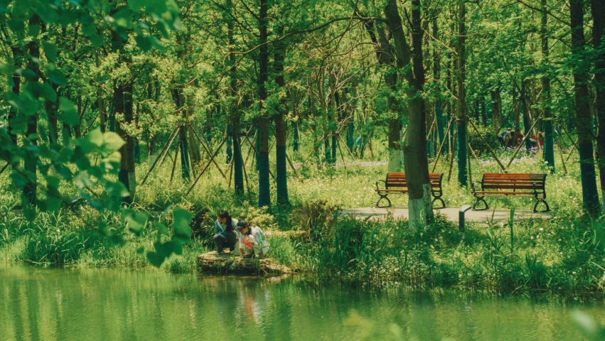 two people standing on the edge of a pond with benches behind them