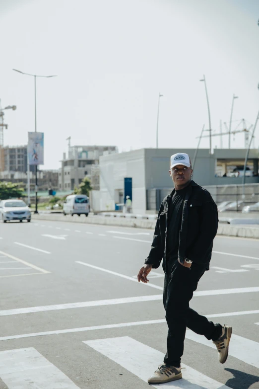 man walking across a crosswalk with a white cap on