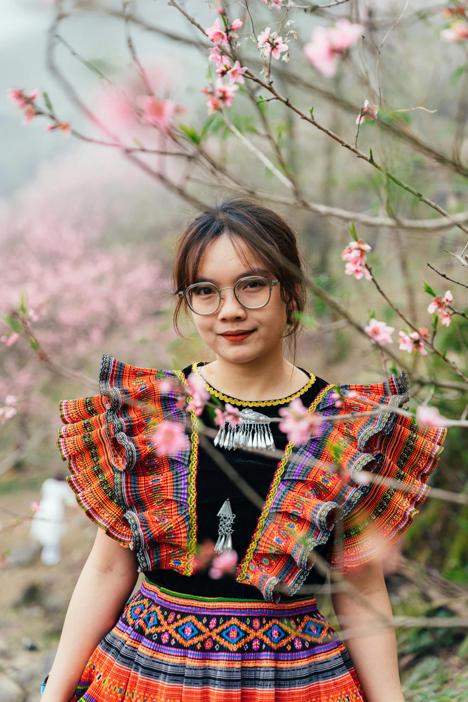 the girl wearing glasses is posing near some pink flowers