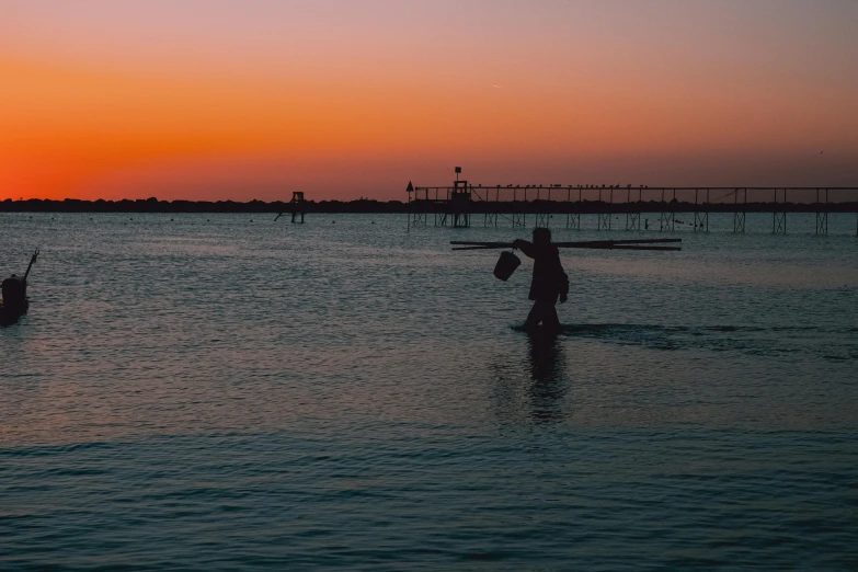 three people are wading through the water at sunset
