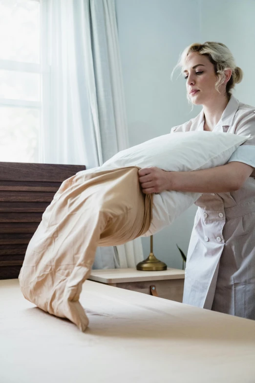 a woman holding a pillow and pulling out the back of an unmade bed