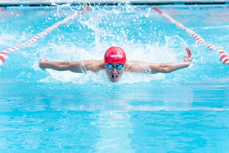 a swimmer wearing a red swim cap and goggles coming out of the water