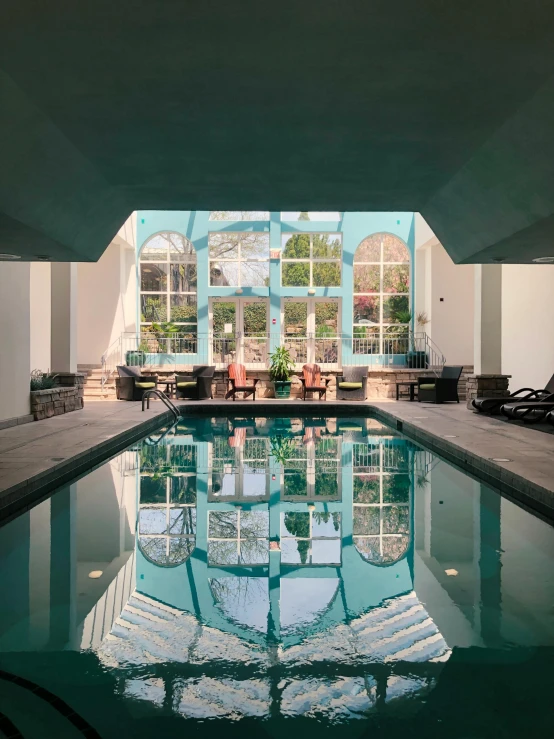 an indoor swimming pool with windows and patio furniture