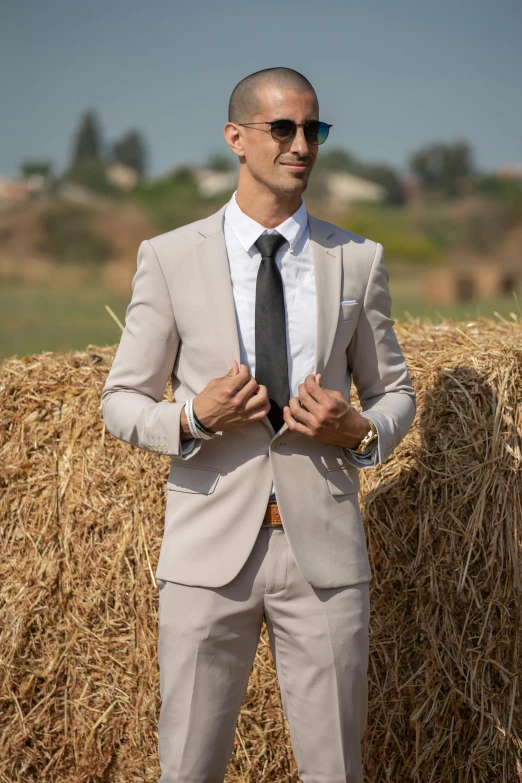 a young businessman standing in front of bales of hay wearing sunglasses and a suit