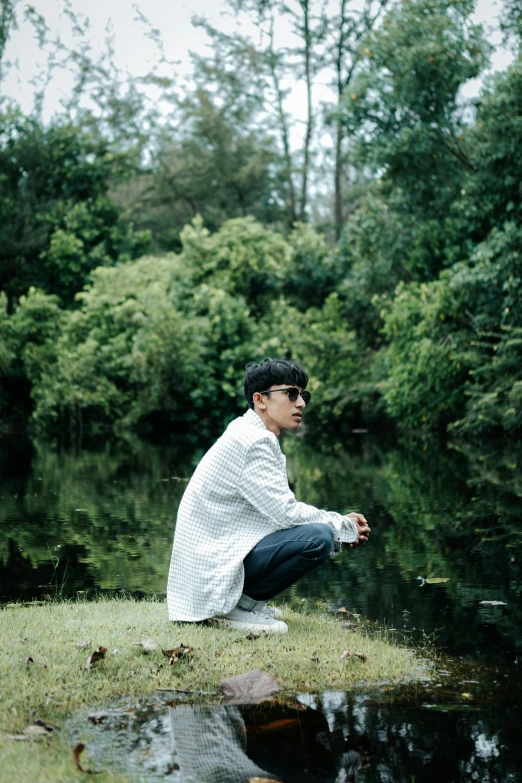 man seated on grassy bank beside small pond in woods