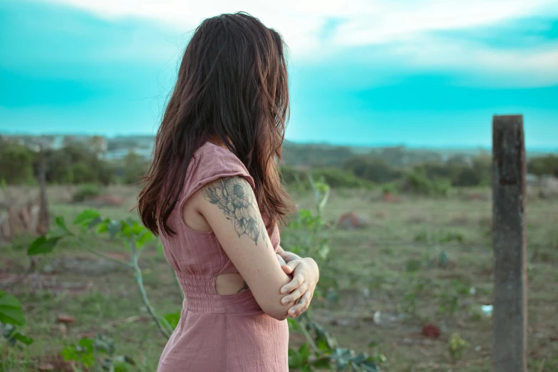 a young woman standing in a field with her arm around a pole