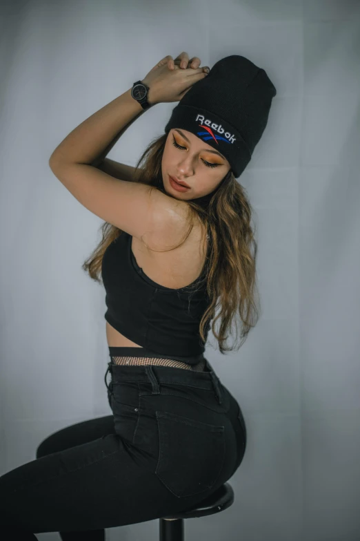 a woman sitting on a stool wearing a black hat