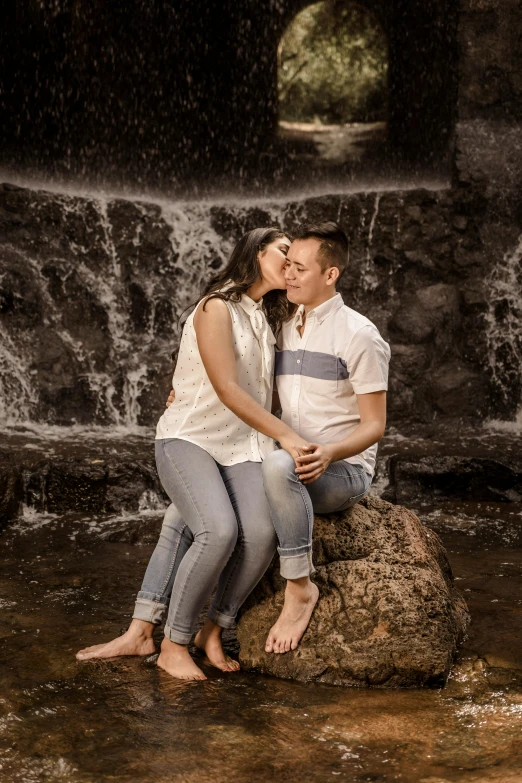 a man and woman kiss each other while sitting on top of a rock by the water