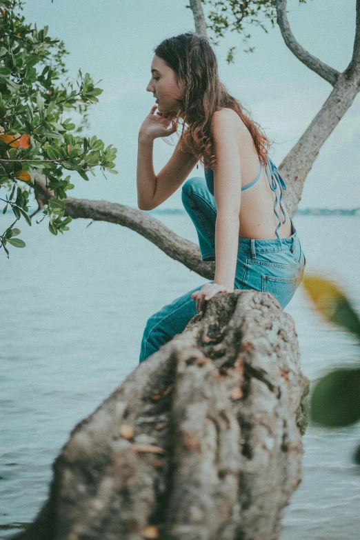 a woman with long hair is sitting on a tree in front of the water
