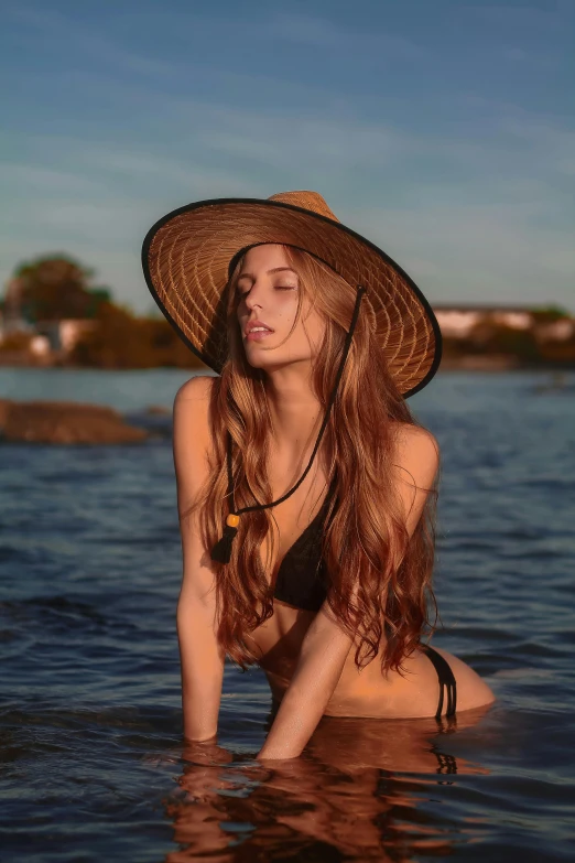 a woman is sitting in the water in a hat