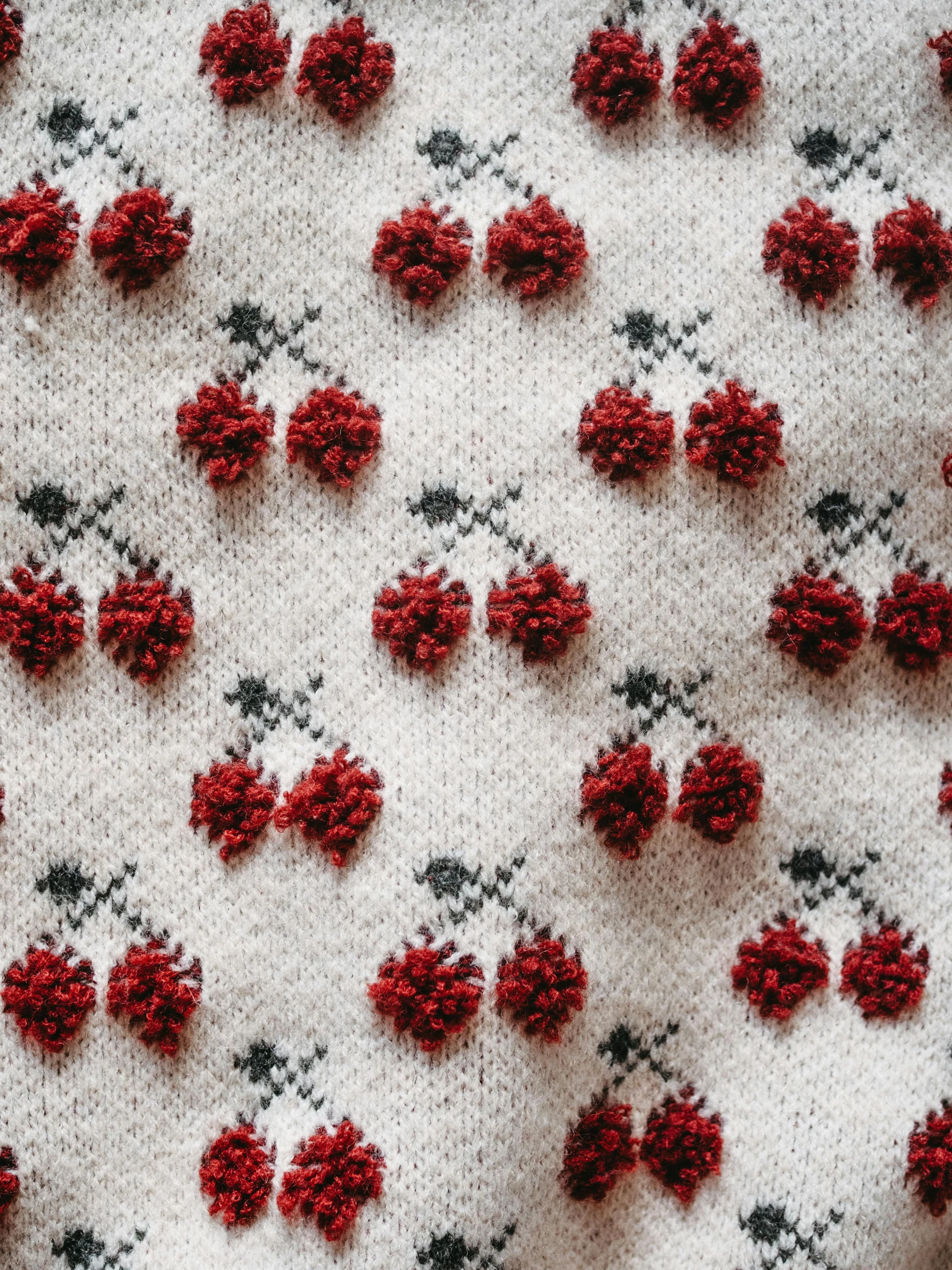 a close up of a crochet surface with a knitted design with red flowers and grey dots