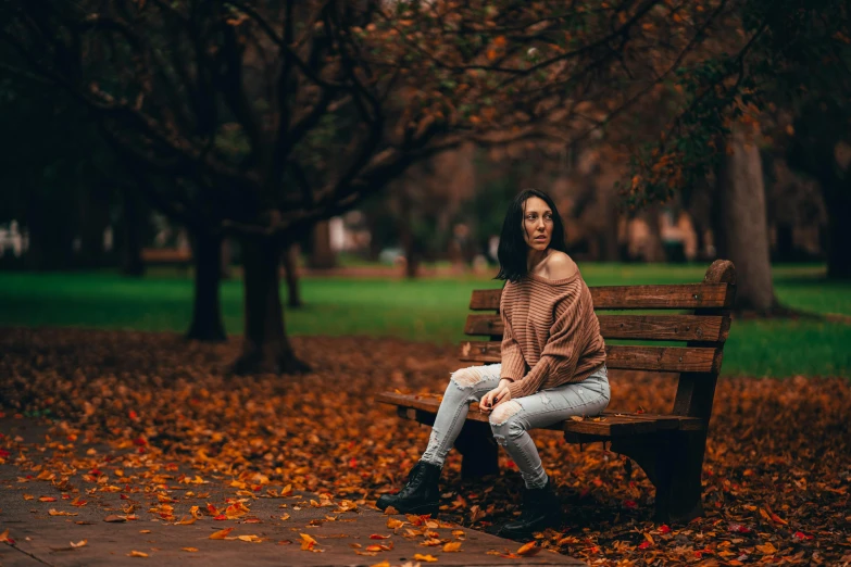 a woman is sitting on a bench outside in the leaves