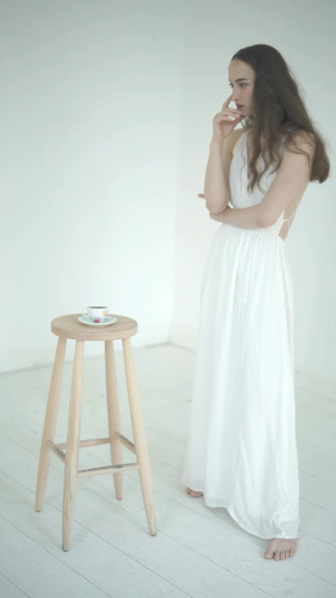 woman in a white dress leaning on a stool with a coffee mug