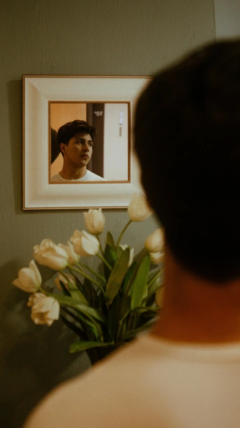 a man in a room with flowers and a framed image