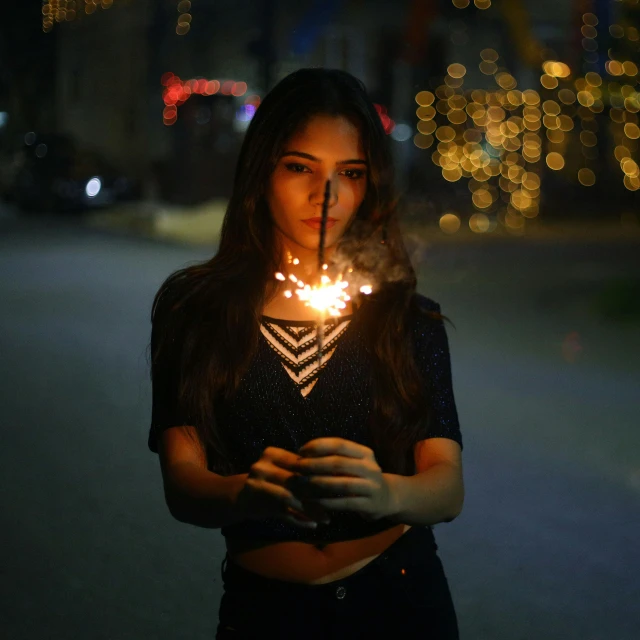 woman in dark clothing standing by road holding sparkler