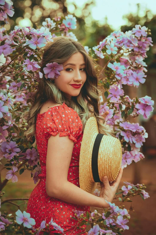 a beautiful woman standing near purple flowers and holding her hat