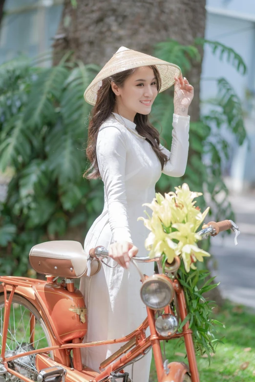 a woman is holding her hat standing next to an old - fashioned bicycle