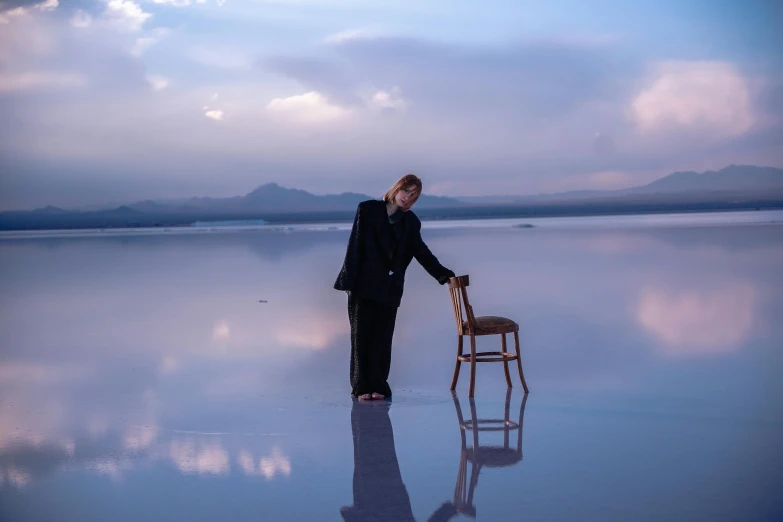 a man in a suit is standing beside a chair on a lake