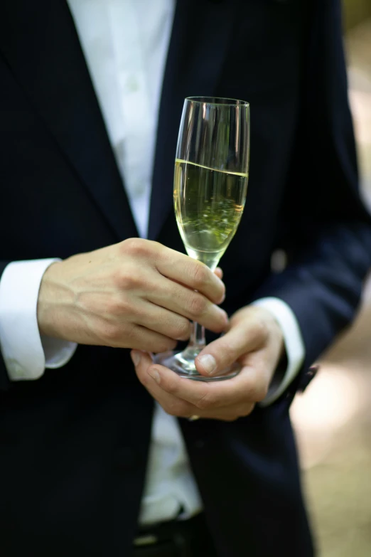 a man in a black suit holds a glass of champagne