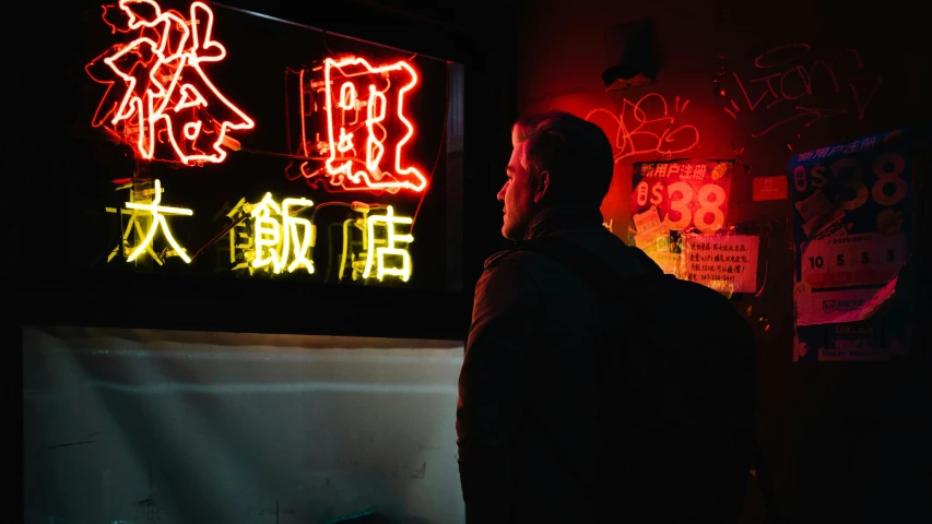 a man stands near a neon sign in an oriental language