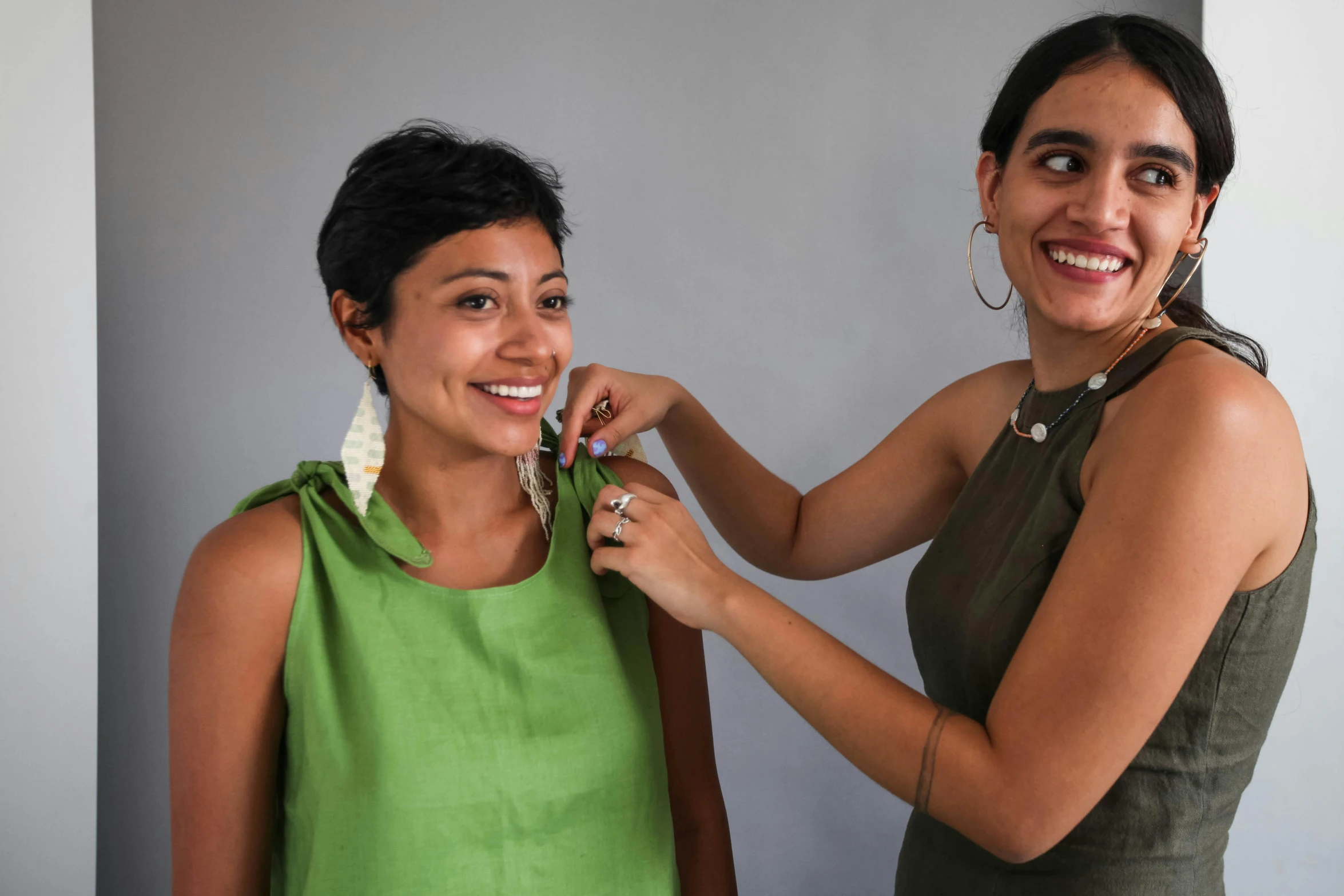 a woman putting jewelry on another woman's neck