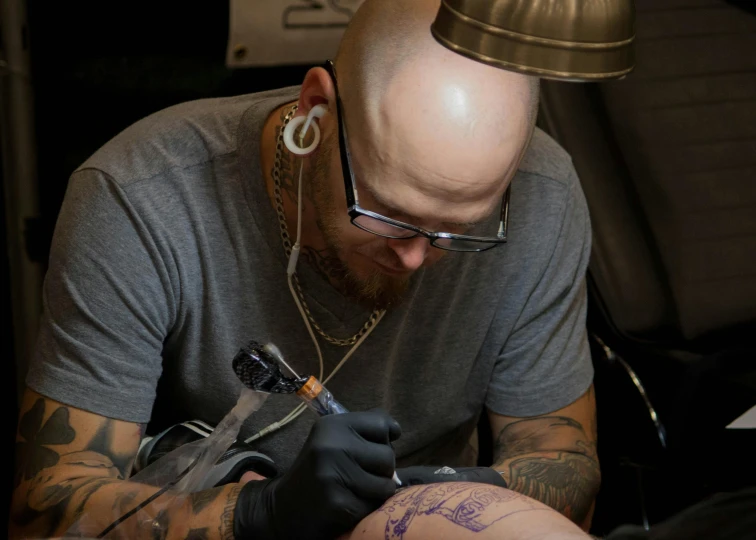 a bald man is  someone's arm and getting a tattoo